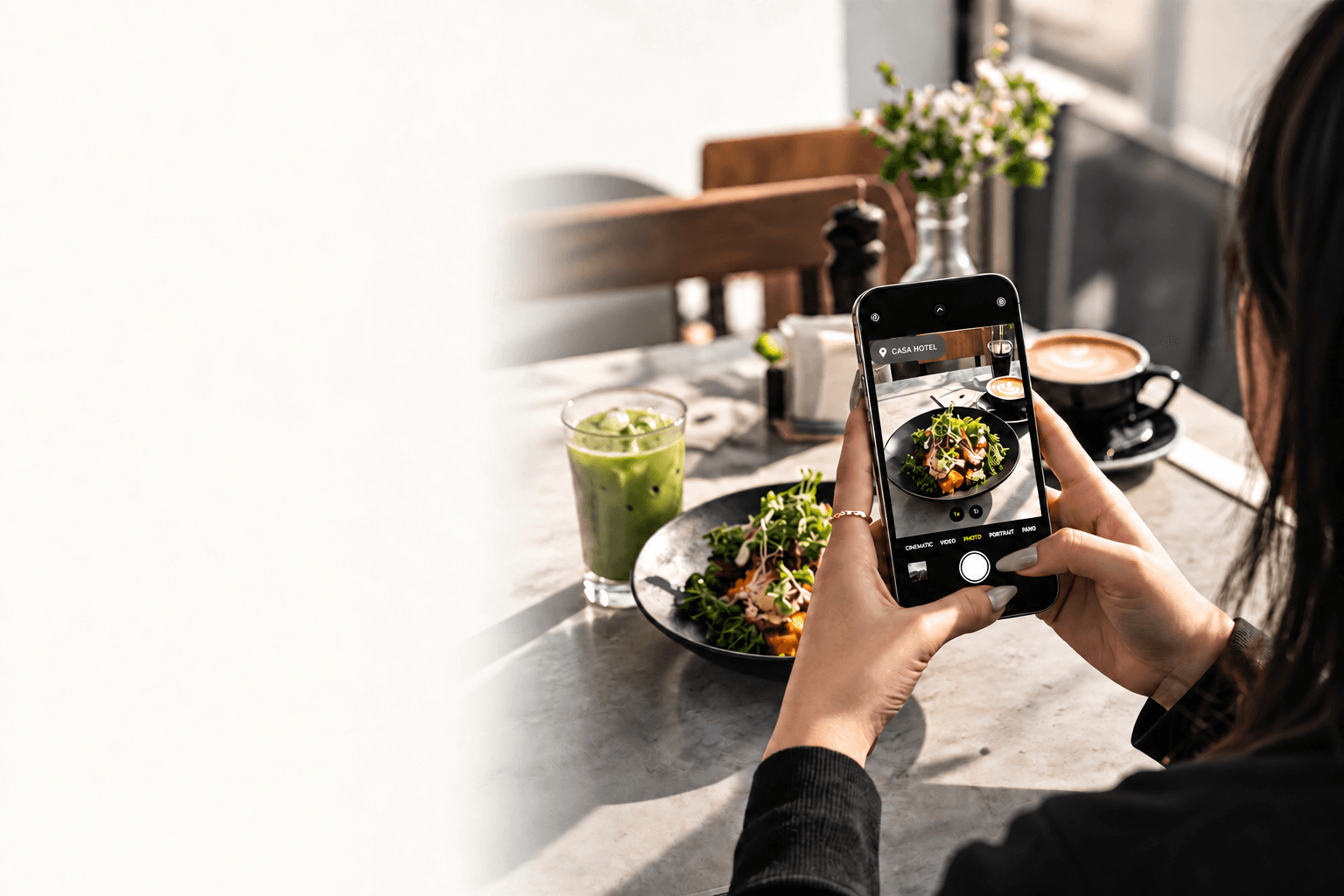 A customer photographing a meal with their phone in a sunlit restaurant